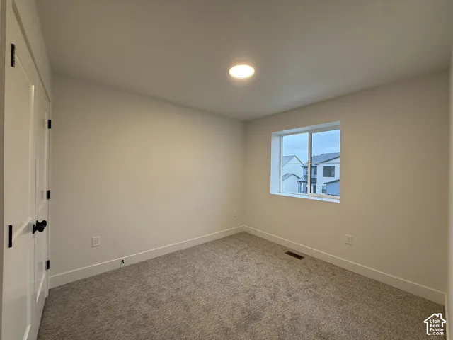 Recessed ceiling lighting, a single window, white trim, a solid panel door with dark hardware, and neutral carpeting