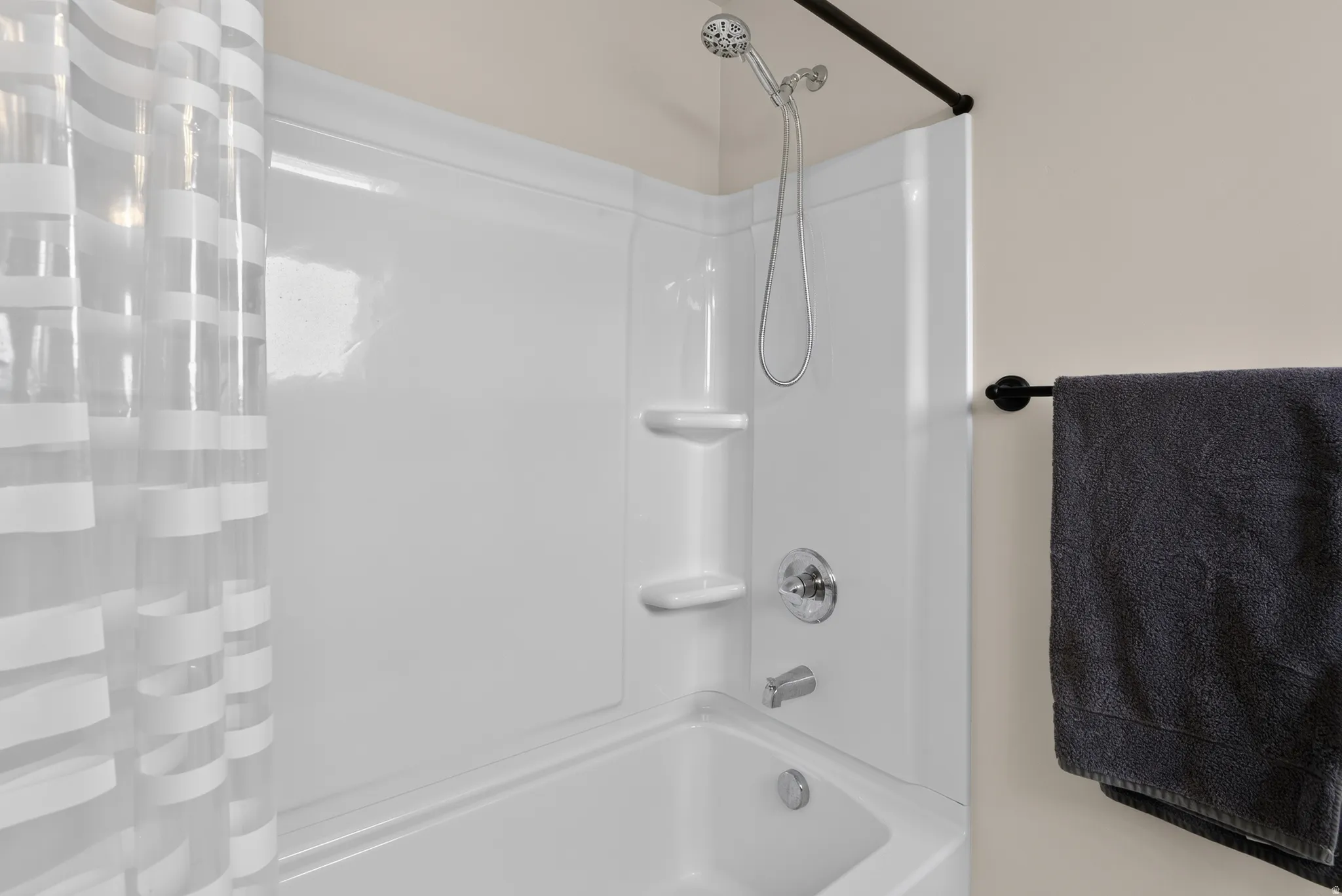 White tub and shower combination with chrome fixtures, integrated shelving, and a handheld showerhead