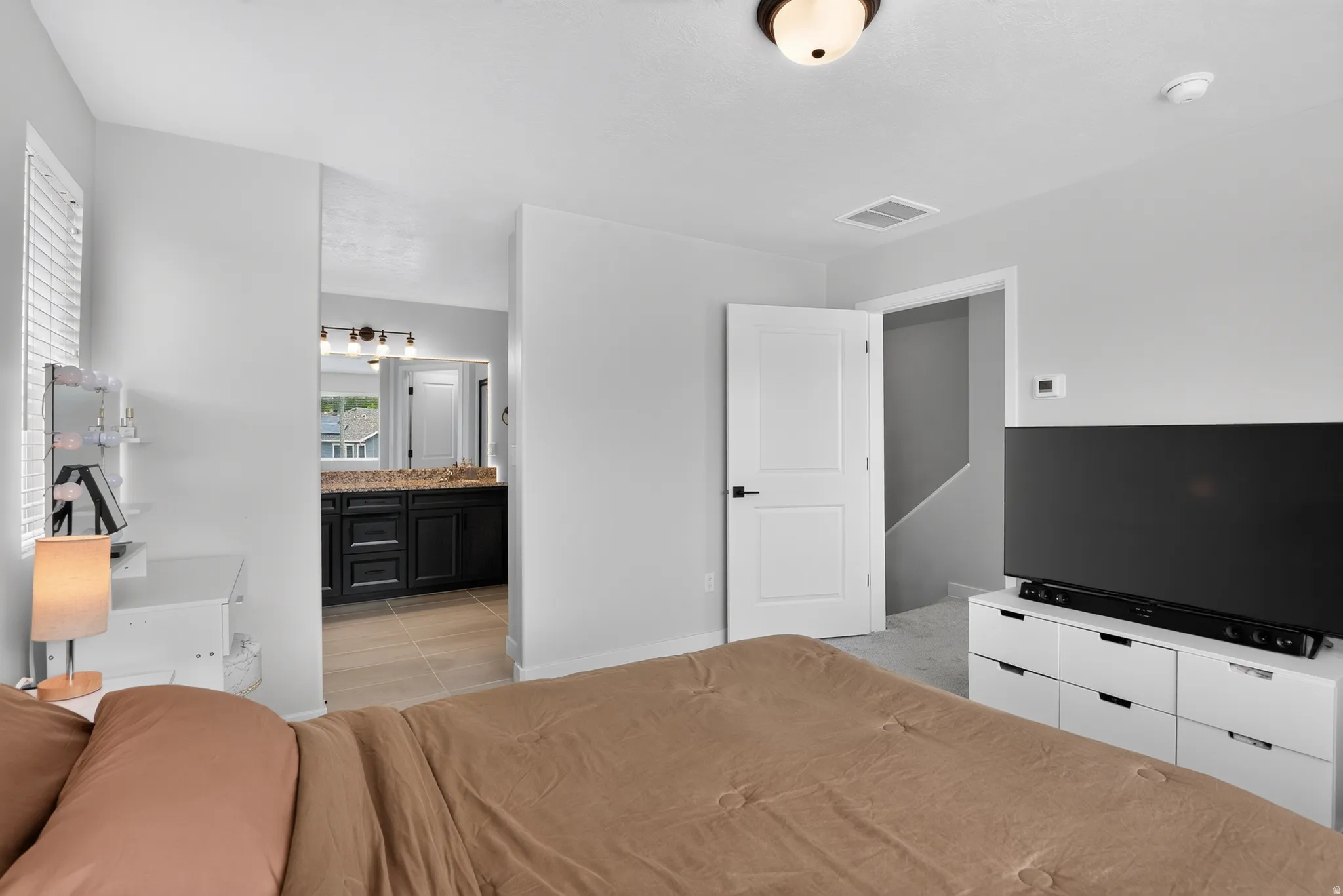 Bedroom featuring a white paneled door with black hardware, a ceiling-mounted light fixture, and a window with blinds