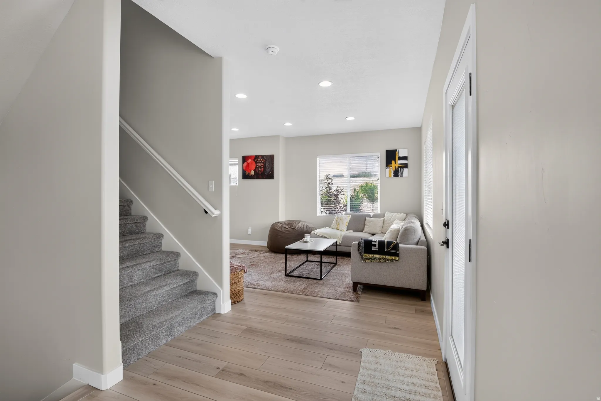 Open-concept living space featuring wood-finish flooring, recessed lighting, and a carpeted staircase with a white handrail