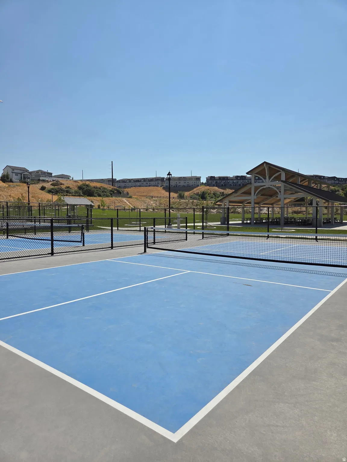 Recreational area featuring multiple blue-surfaced pickleball courts with white line markings and black netting