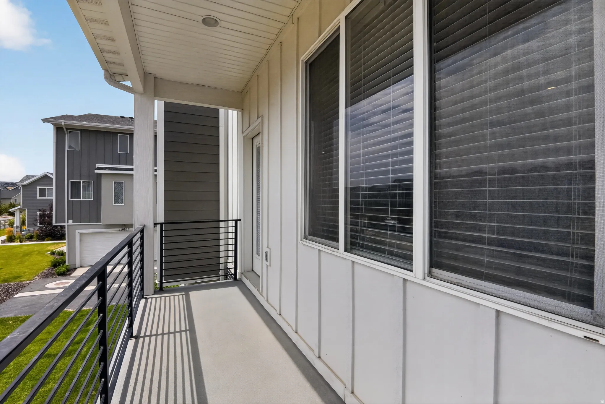 Covered balcony with linear black railings, vertical white siding, and a white framed door