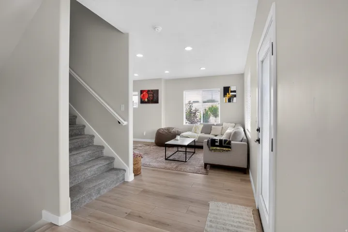 Open-concept living space featuring wood-finish flooring, recessed lighting, and a carpeted staircase with a white handrail