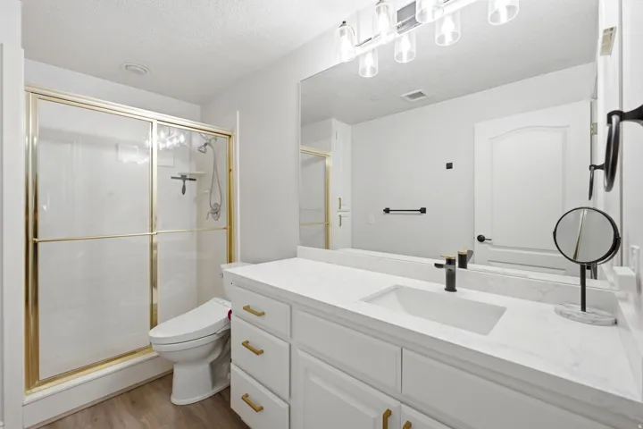 Primary bathroom featuring a updated quartz countertops, sink and fixture, gold-framed glass shower enclosure.