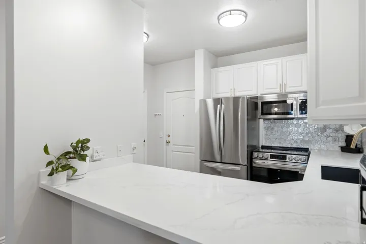 The kitchen sits just inside the front door with stainless steel appliances, beautiful tile backsplash, and light-toned quartz countertops.