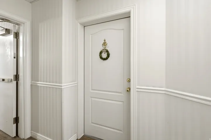 Welcome home! Entrance to condo 107. Interior door with brass hardware, framed by white millwork and striped wallpaper above wainscoting