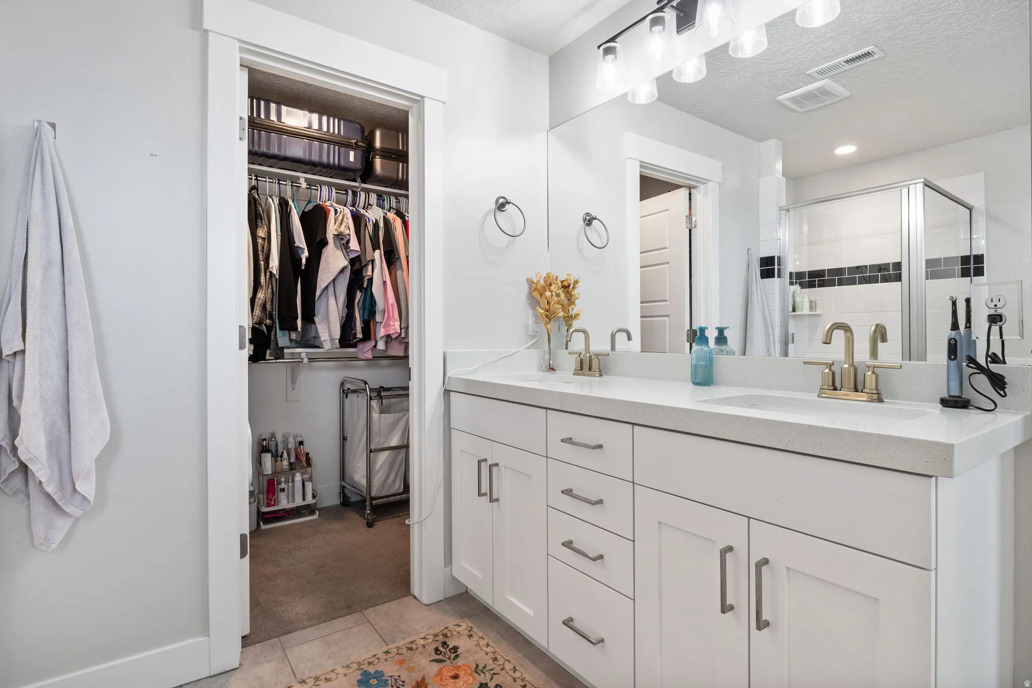 Dual vanity featuring white shaker cabinetry, an integrated white countertop, and brushed brass fixtures
