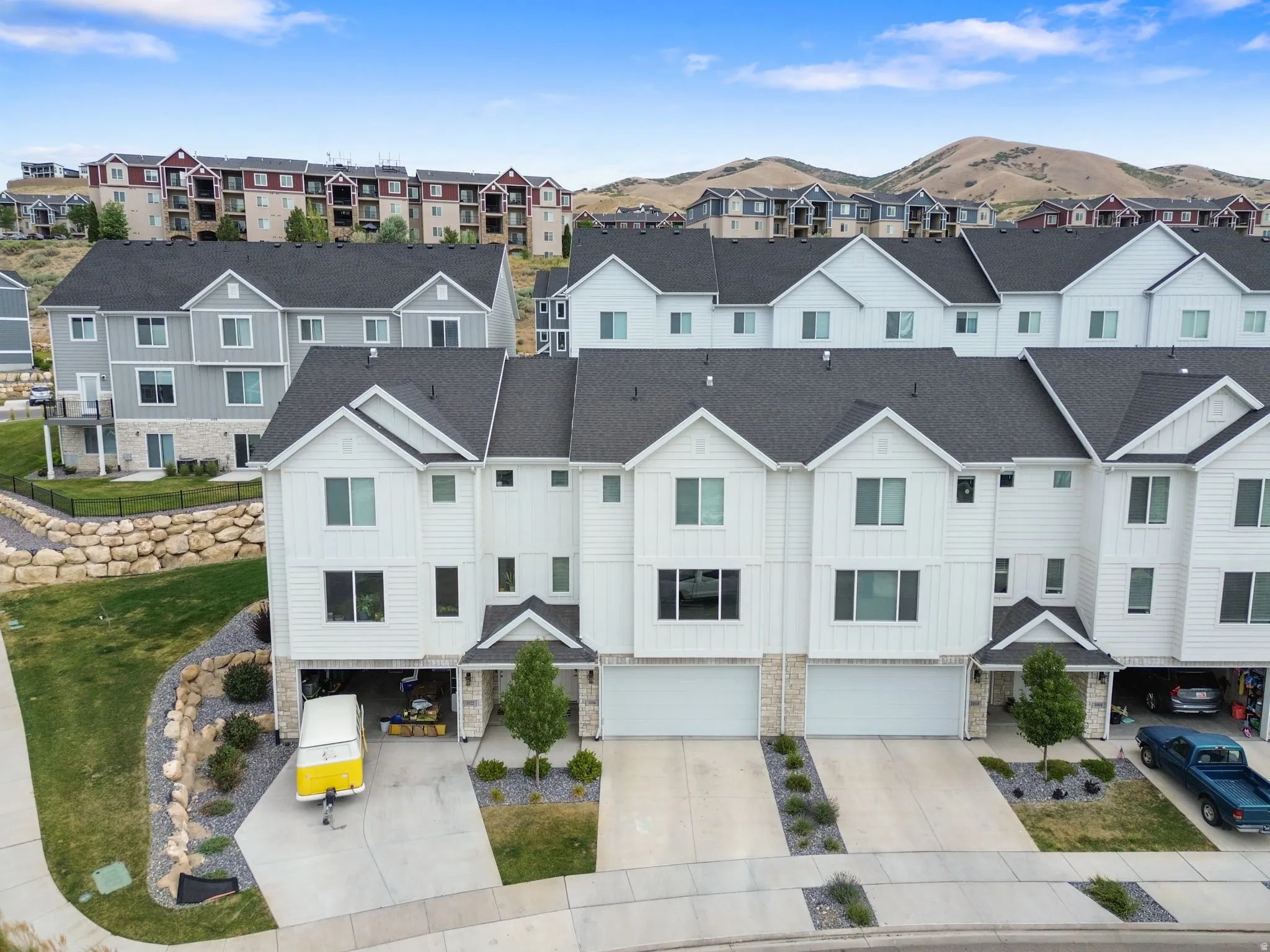 Townhome exterior featuring white siding, dark shingle roofing, attached two-car garage, and stone accents