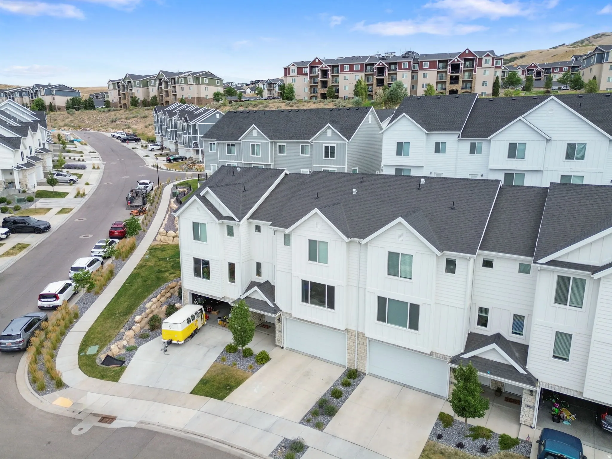 Modern townhome exterior featuring white vertical siding, dark gray roofing, a two-car garage, stone veneer accents, and a covered entry