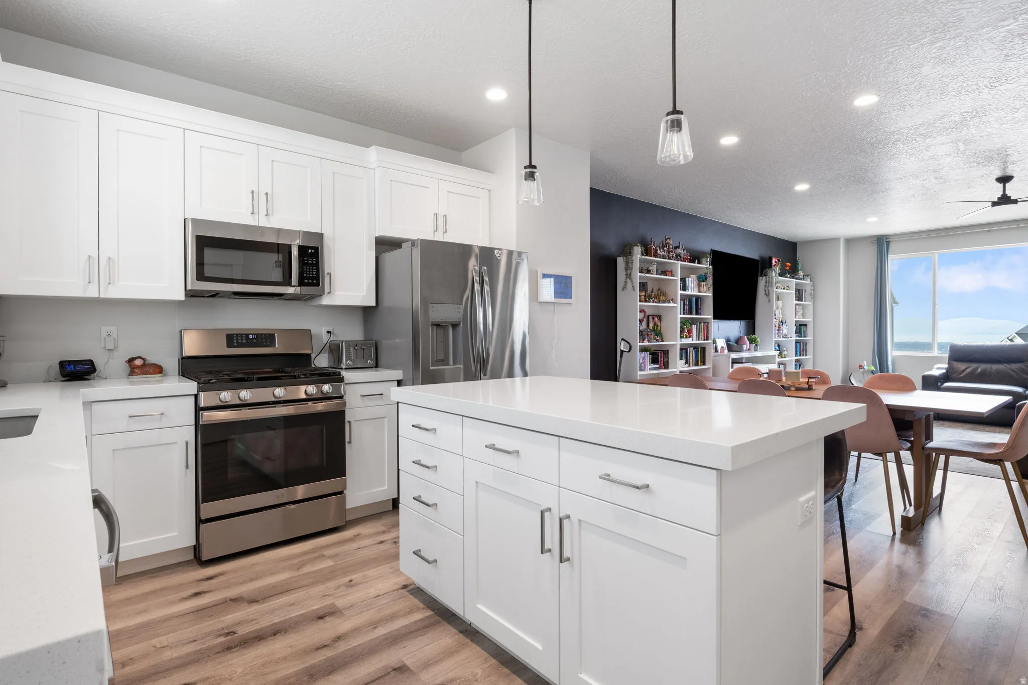 Modern kitchen featuring white shaker cabinetry, stainless steel appliances, a center island with countertop seating, and wood-finish flooring