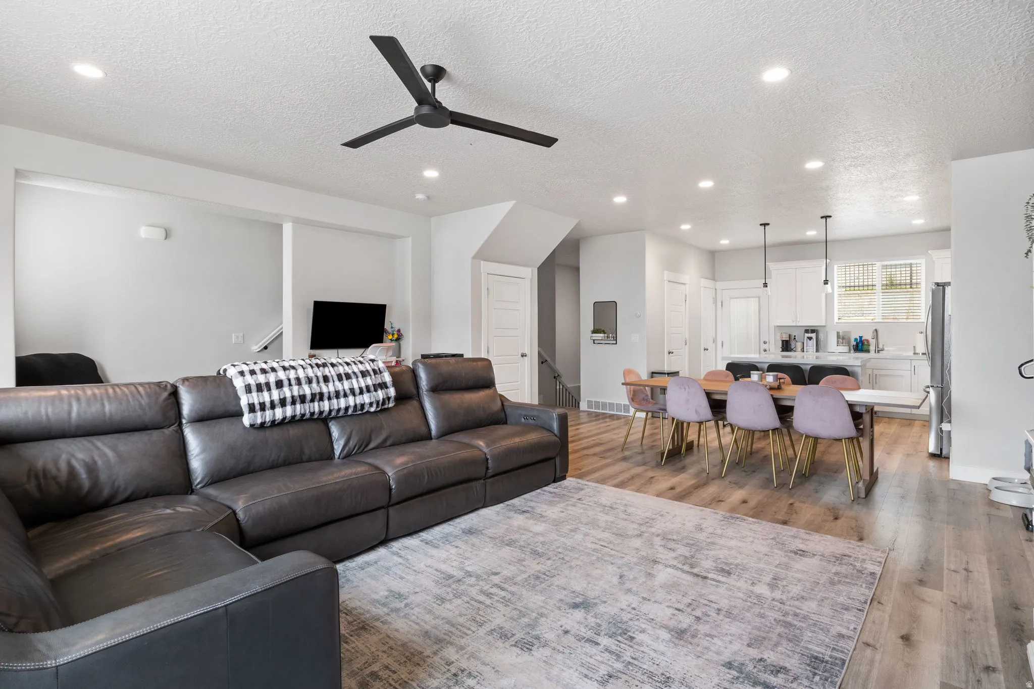 Open-concept living space featuring wood-finish flooring throughout, recessed lighting, and a modern black ceiling fan