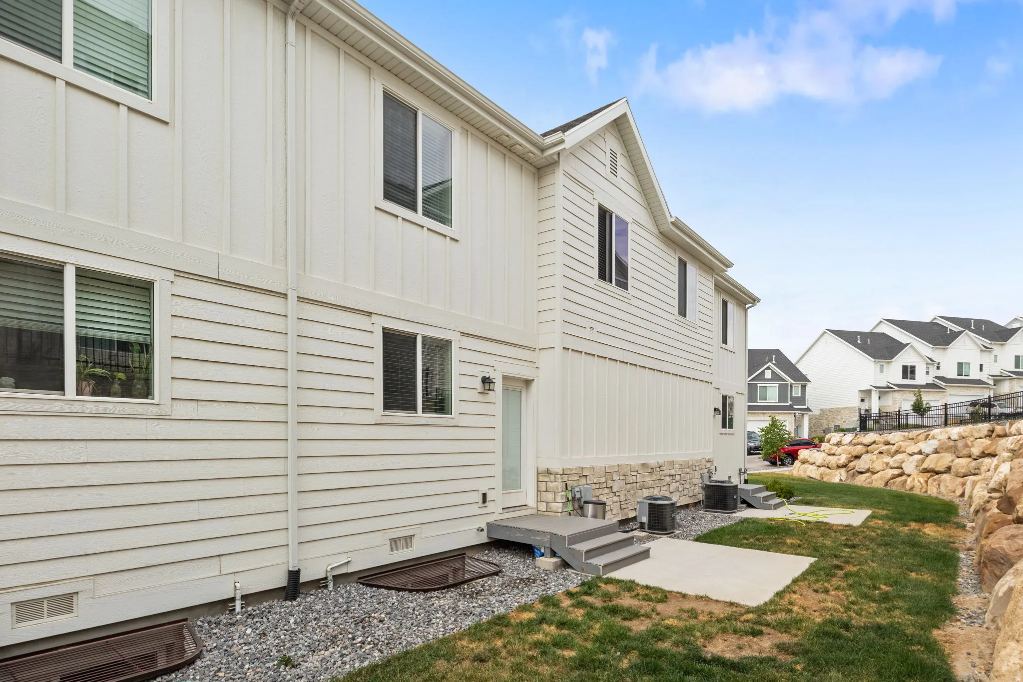 Rear exterior showcasing white horizontal and vertical siding, a stone-clad foundation, and multiple windows with white frames