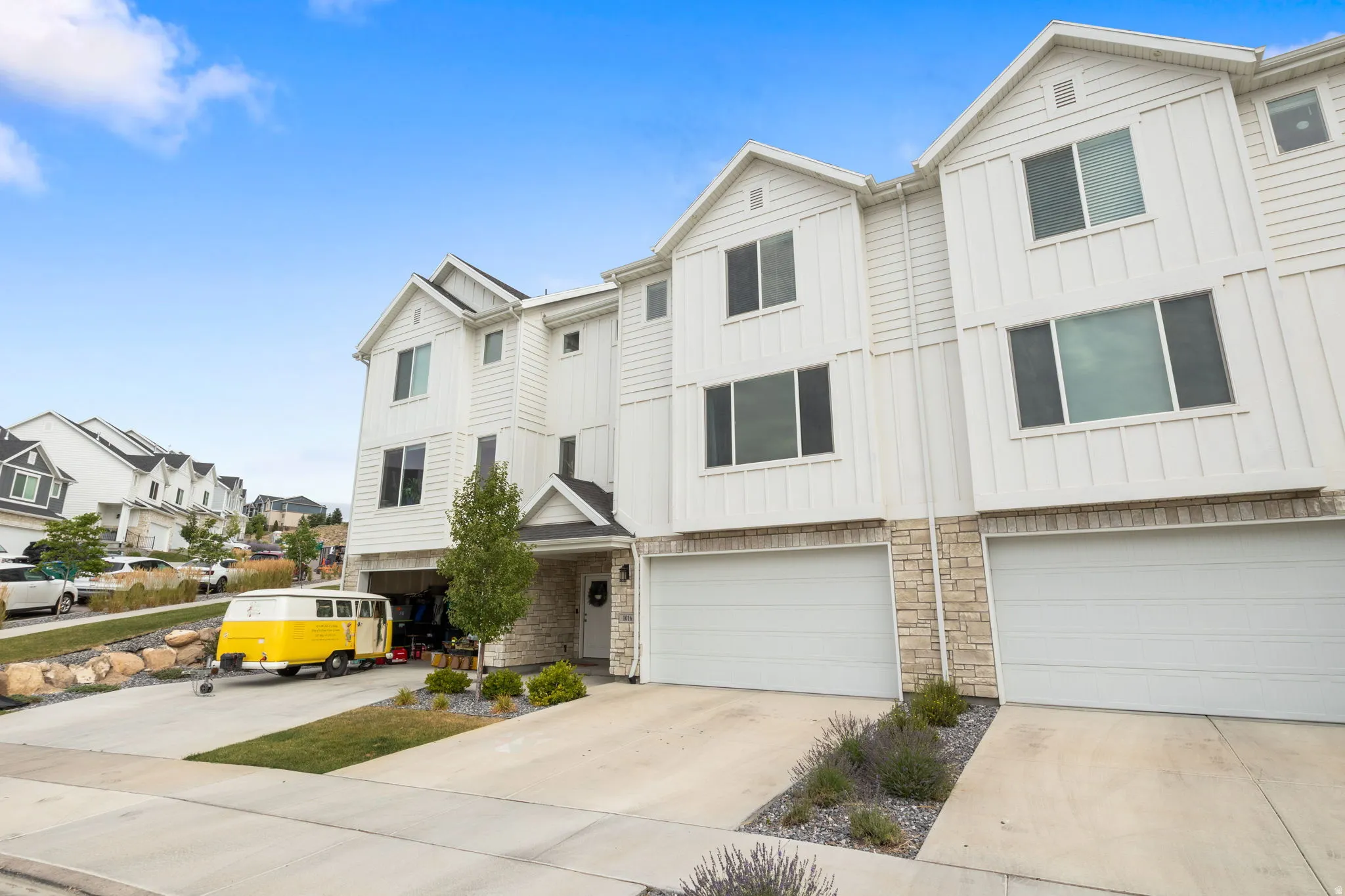 Contemporary multi-story exterior with white vertical and horizontal siding, stone veneer accents, and an attached two-car garage