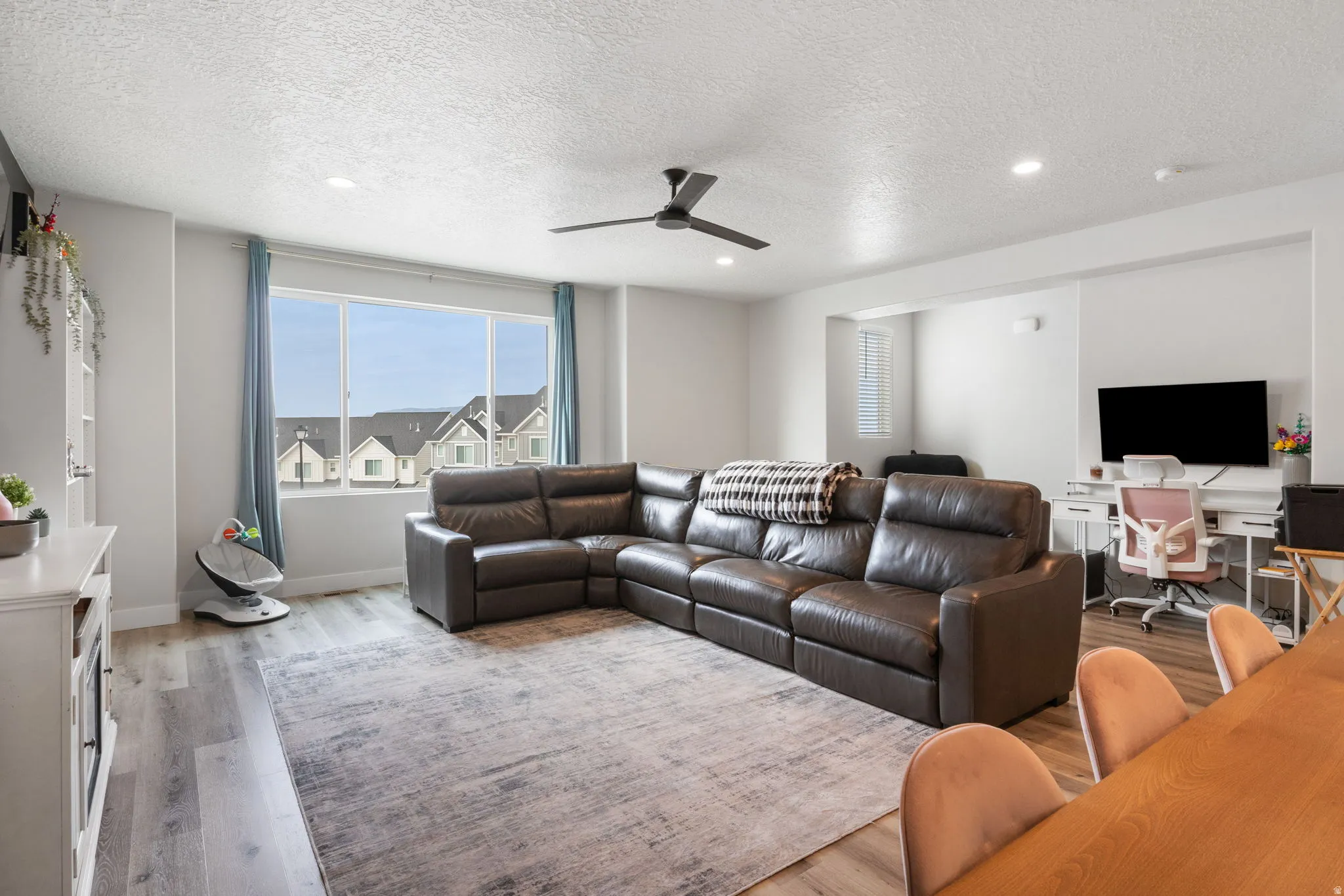 Spacious living area featuring large windows with natural light, recessed ceiling lighting, a ceiling fan, and wood-finish flooring