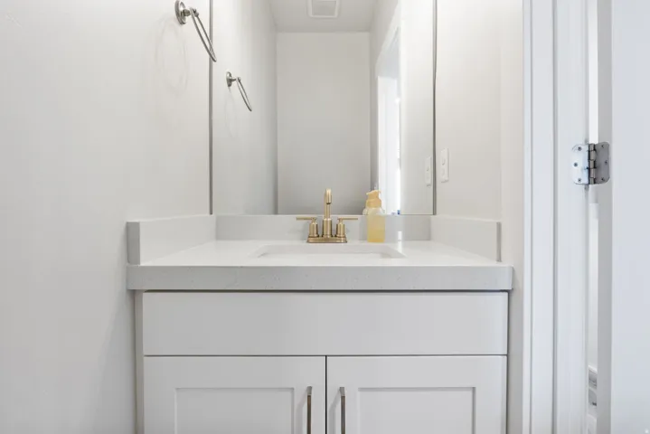 White vanity with shaker-style cabinet doors, brushed gold faucet, integrated sink, and light-toned solid surface countertop