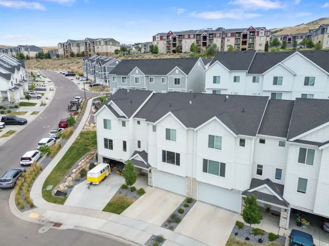 Modern townhome exterior featuring white vertical siding, dark gray roofing, a two-car garage, stone veneer accents, and a covered entry