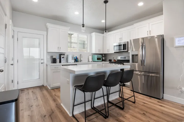 Modern kitchen featuring white shaker cabinetry, stainless steel appliances, a center island with countertop seating, wood-finish flooring, and pendant lighting