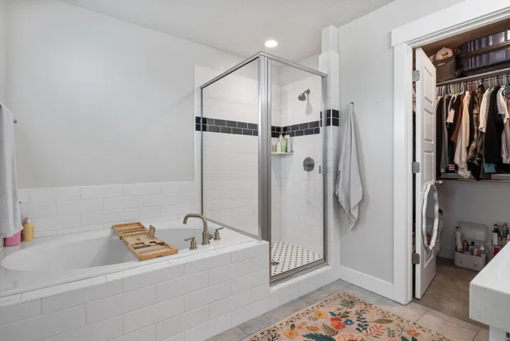 Bathroom featuring a built-in soaking tub with subway tile surround, a glass-enclosed shower with subway tile walls and black accent band, a rain shower head, and a walk-in closet with built-in shelving and hanging rods