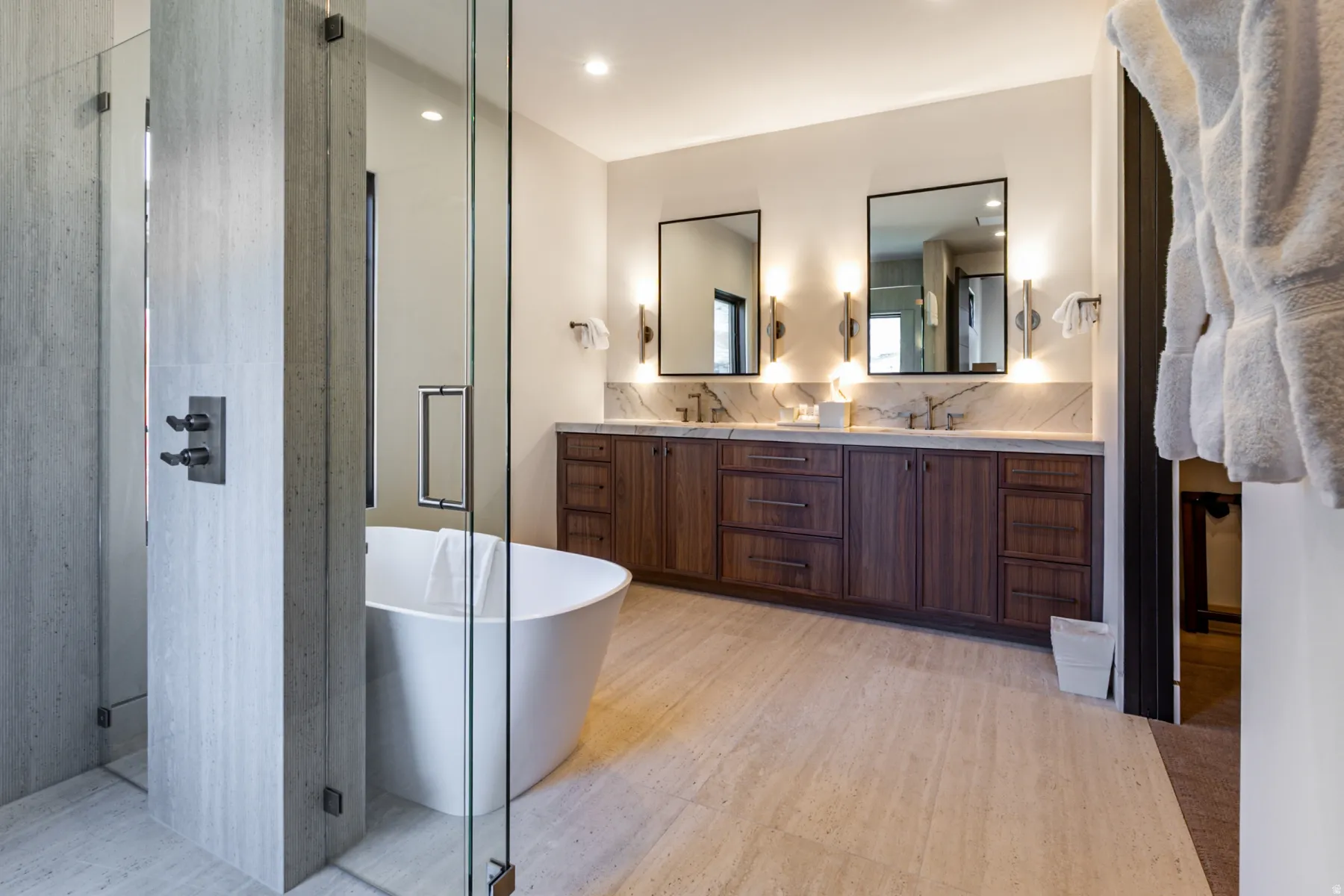Spacious bathroom featuring a freestanding soaking tub, dual vanity with undermount sinks, stone countertop with matching backsplash, and wood-finish cabinetry