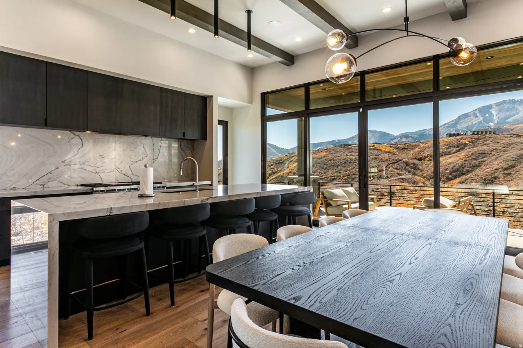 Modern kitchen and dining area featuring floor-to-ceiling glass doors, revealing a mountain landscape