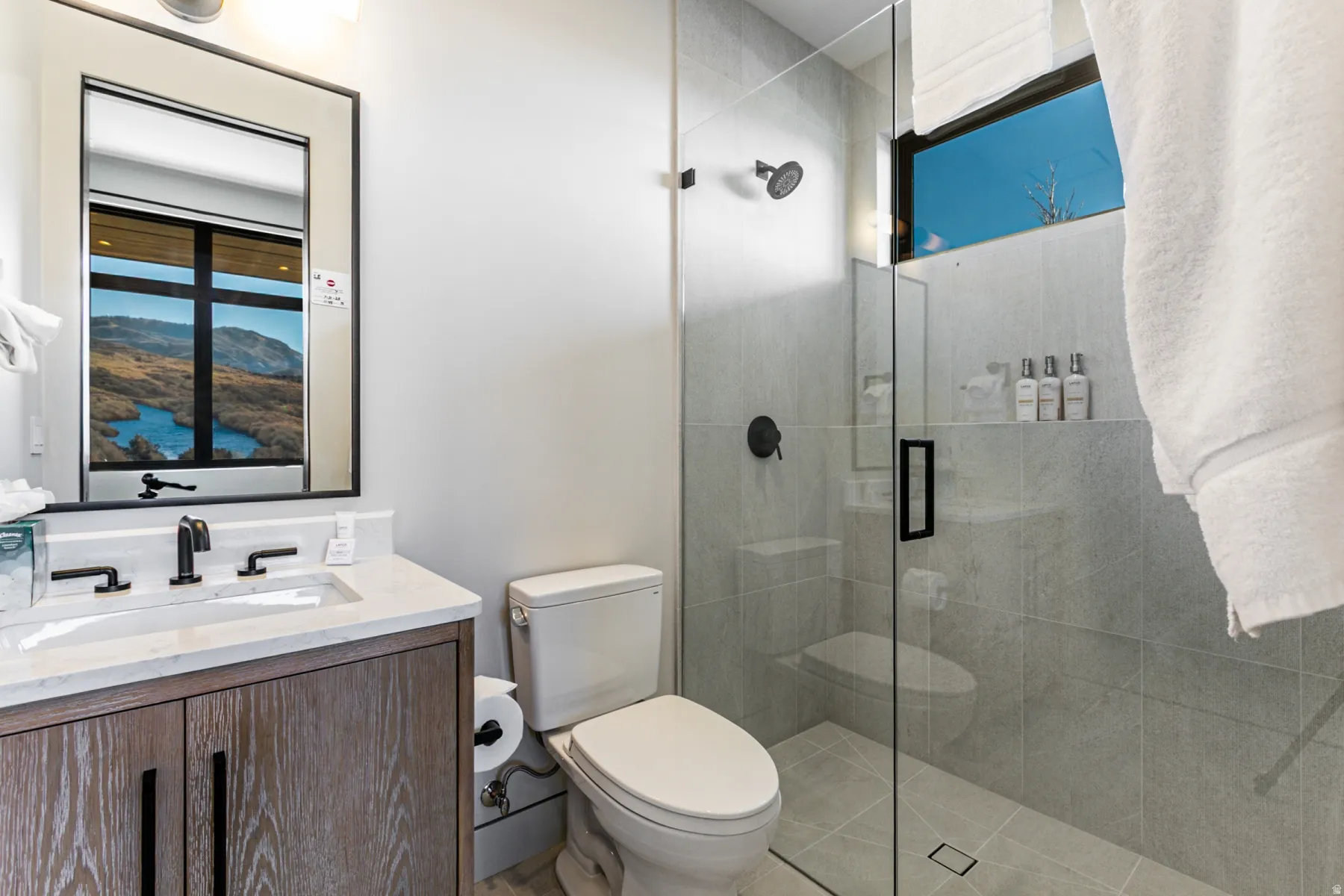 Contemporary bathroom featuring a floating wood-finish vanity with a rectangular sink, a stone countertop, and matte black fixtures