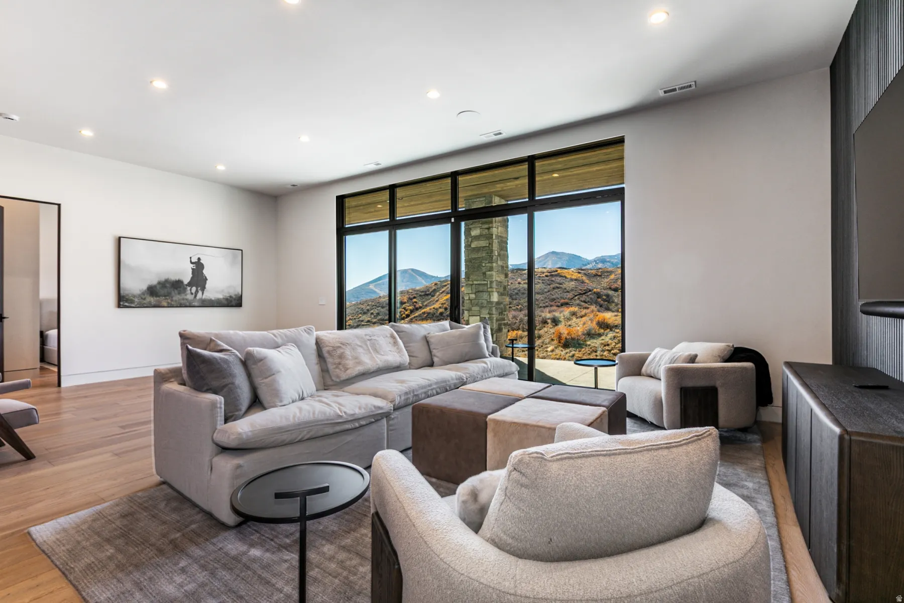 Spacious living area featuring expansive windows with mountain scenery, recessed ceiling lighting, and wood-finish flooring