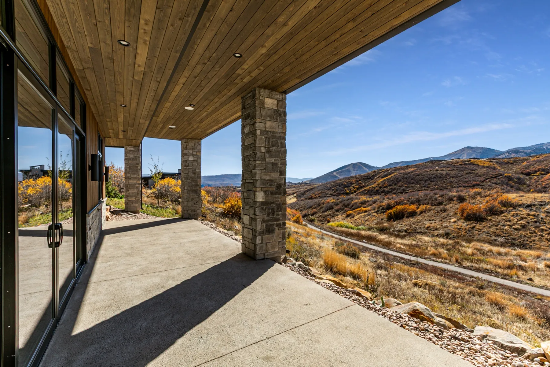 Expansive covered patio featuring a concrete surface, wood-finish ceiling, recessed lighting, and stone-clad support columns