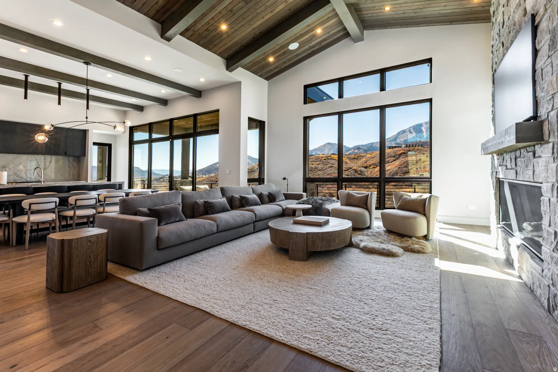 Spacious living area featuring large picture windows, a stone-clad fireplace with a substantial mantel, and wood-finish flooring