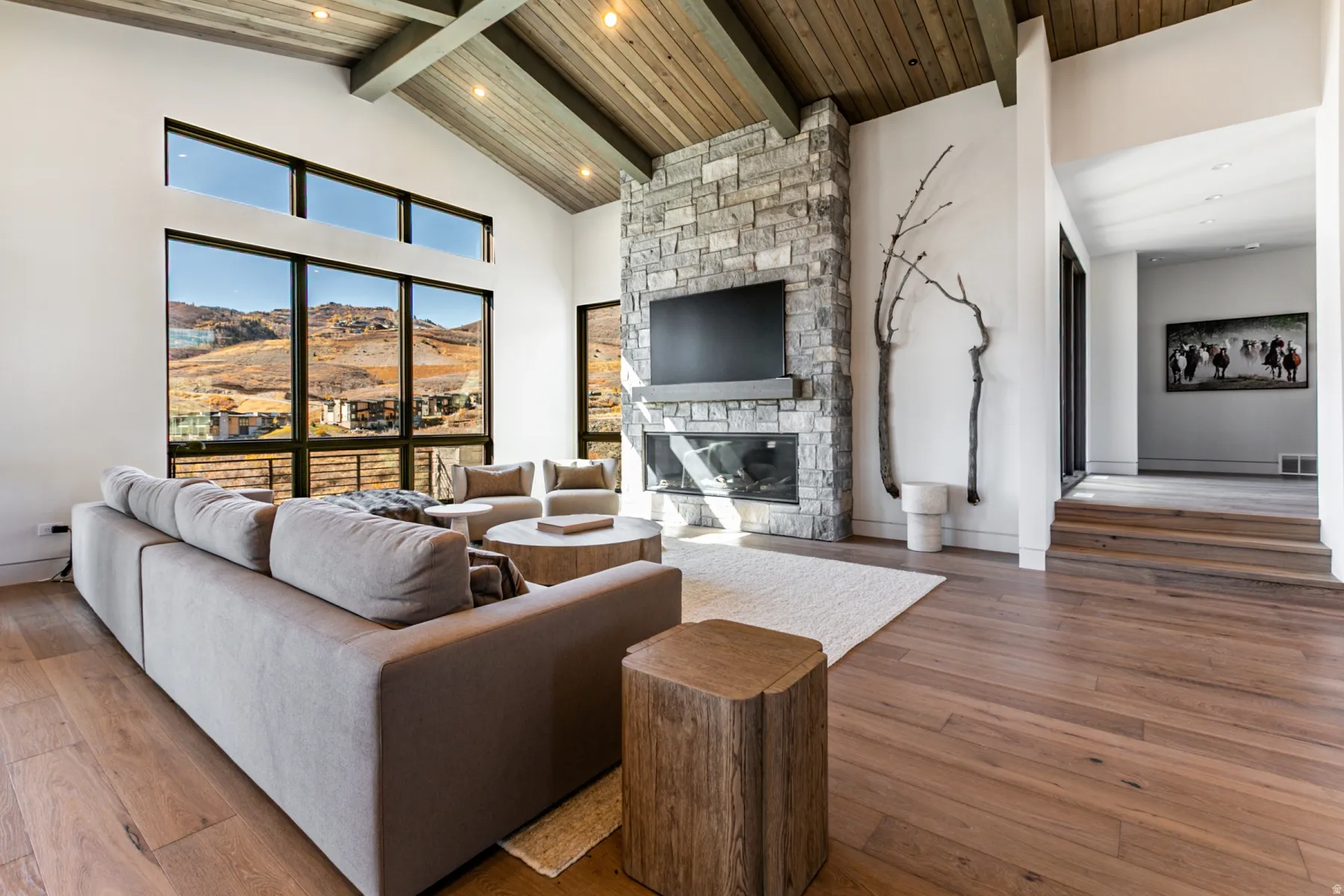 Spacious living area featuring expansive windows, a prominent stone fireplace, vaulted wood-paneled ceilings, wood-finish flooring, and a multi-level entryway