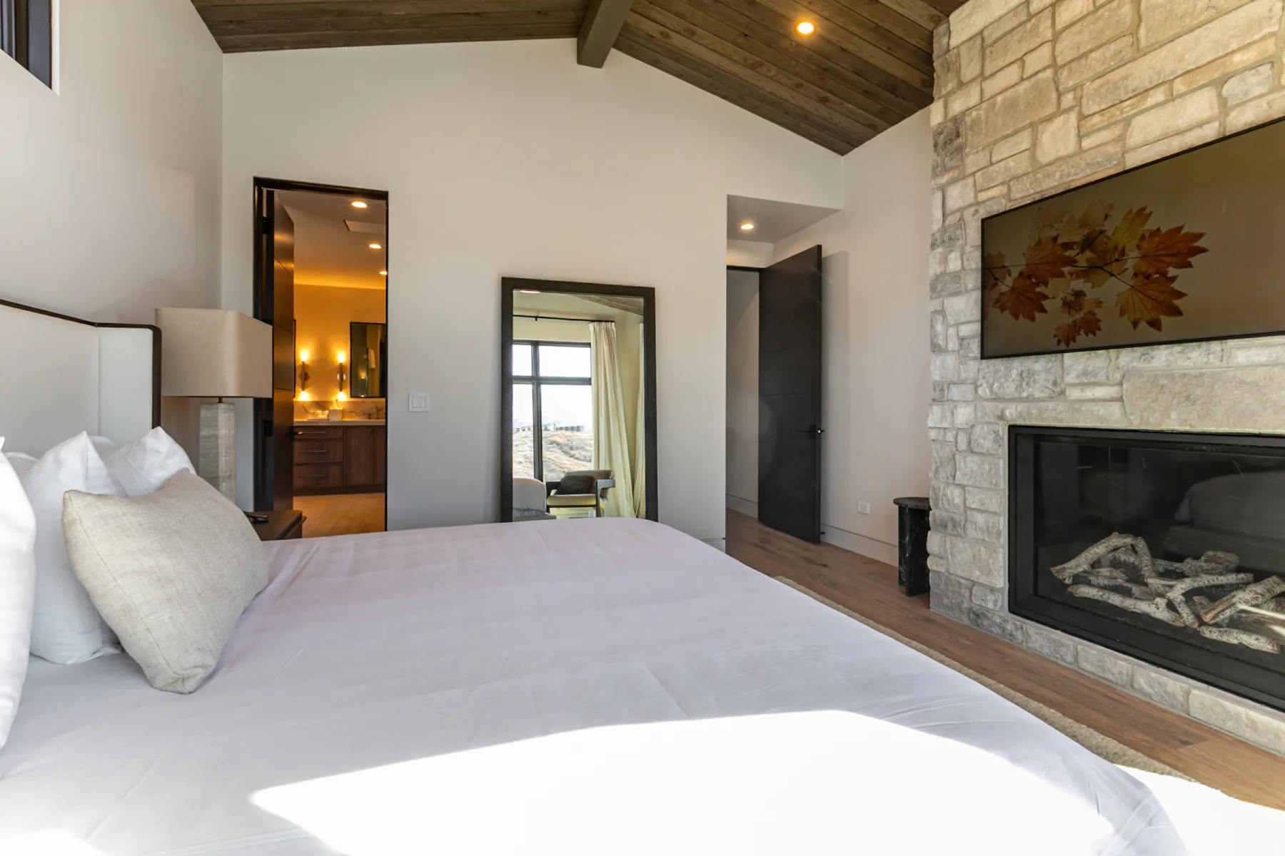 Spacious room featuring a stone-clad fireplace with a built-in television, wood-finish flooring, and a vaulted wood-paneled ceiling