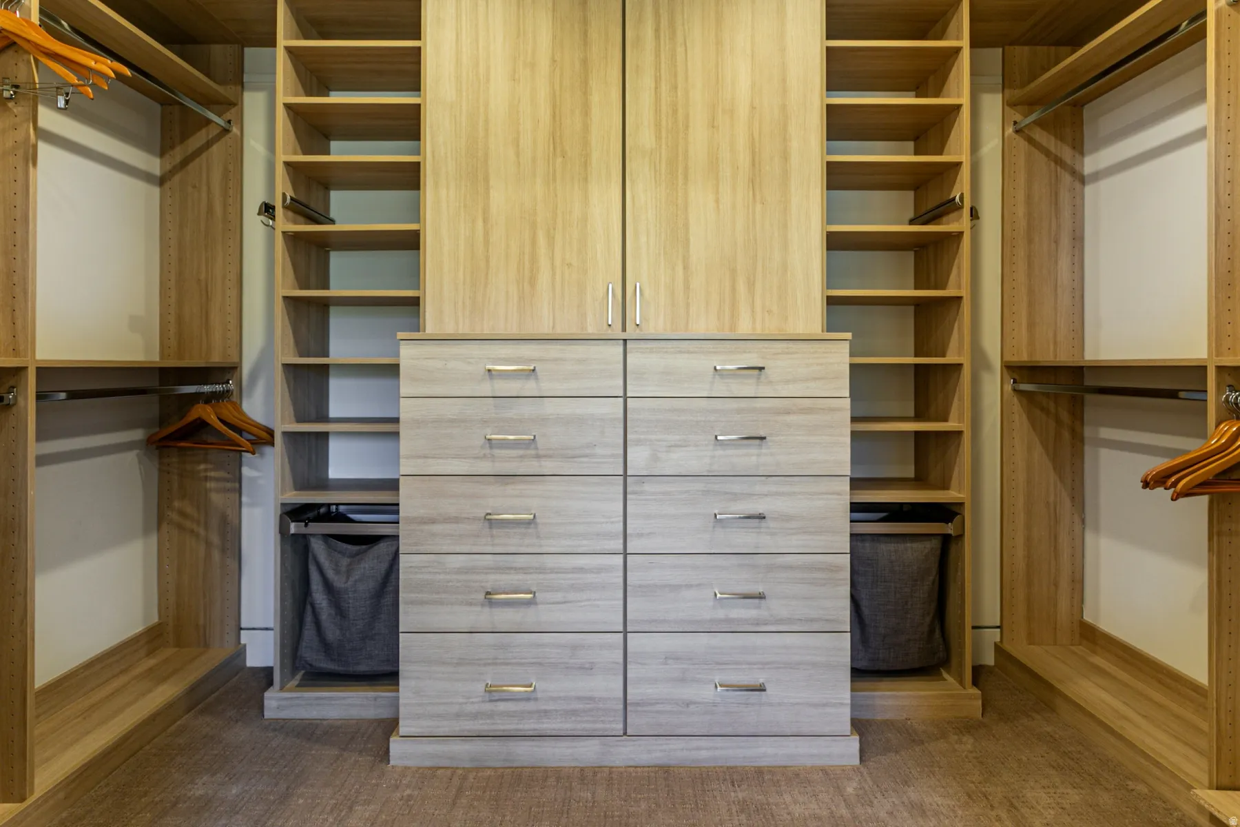 Custom closet system featuring light wood-finish cabinetry, extensive shelving, and multiple hanging rods