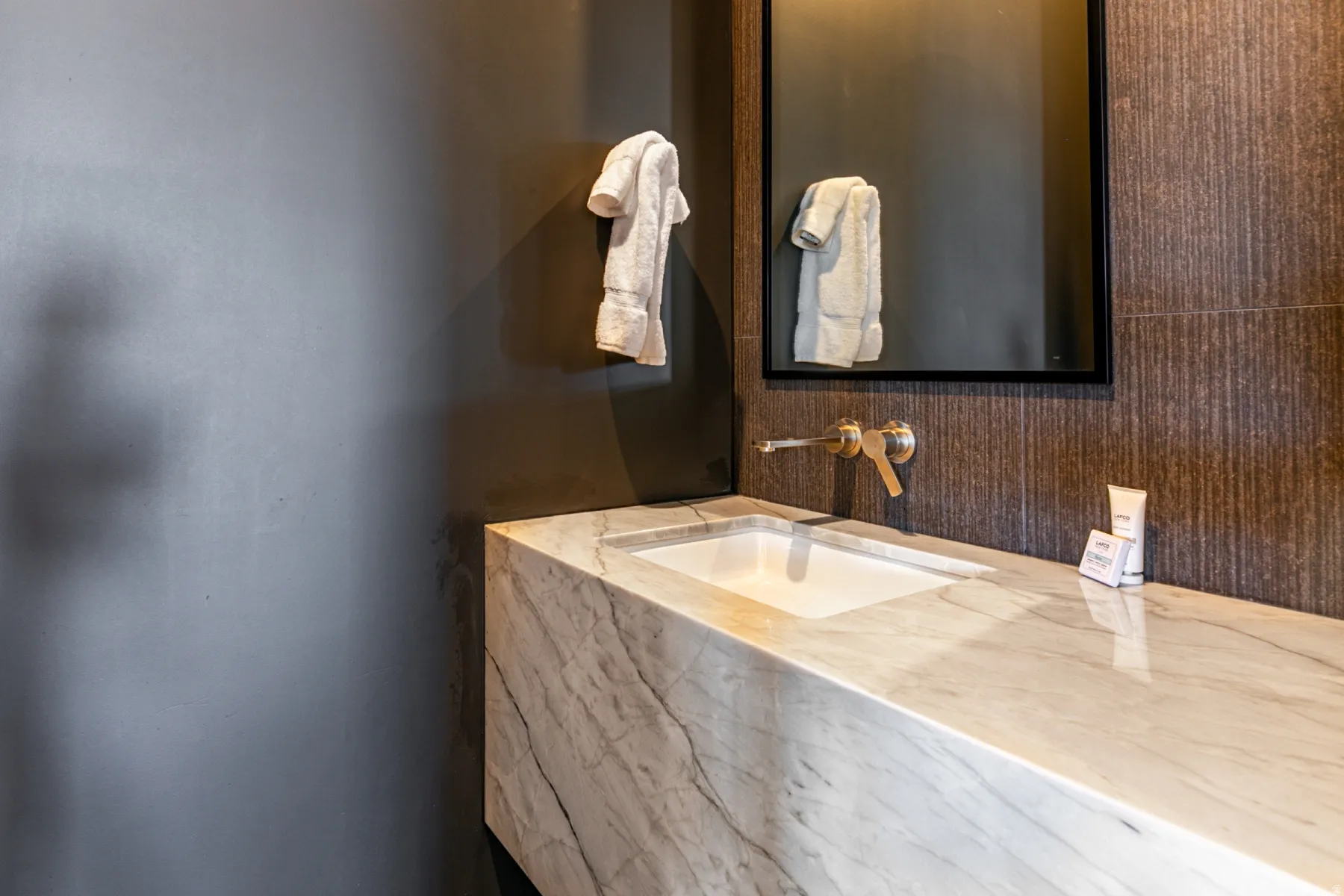 Integrated marble vanity with an undermount sink, wall-mounted brass faucet, and a black-framed mirror over textured wall tile
