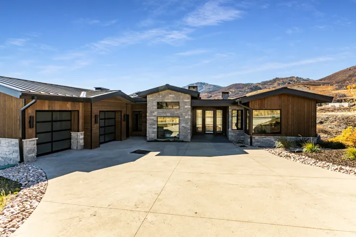 Contemporary exterior featuring wood siding and stone accents, a multi-pane glass entry door, multiple large windows, and a paved driveway