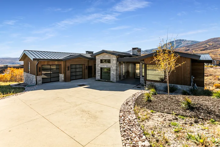 Modern mountain home featuring a stone and wood siding exterior, a metal roof, and a concrete driveway