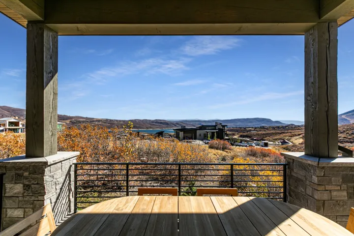 Covered outdoor deck with a round wood-finish table, framed by stone-clad columns and large timber beams