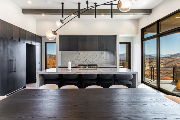 Contemporary kitchen featuring a large central island with seating, dark wood-finish cabinetry, a striking stone slab backsplash, and expansive floor-to-ceiling windows