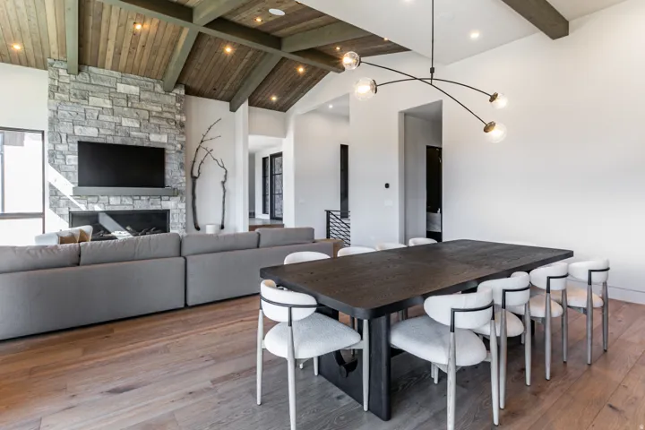 Spacious living area featuring high vaulted ceilings with wood paneling and exposed beams, a stone-clad fireplace, and wood-finish flooring
