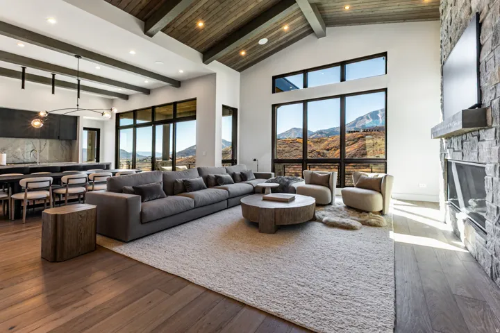Spacious living area featuring large picture windows, a stone-clad fireplace with a substantial mantel, and wood-finish flooring