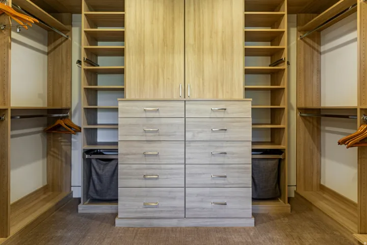 Custom closet system featuring light wood-finish cabinetry, extensive shelving, and multiple hanging rods
