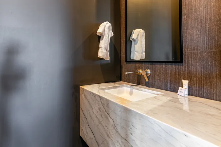 Integrated marble vanity with an undermount sink, wall-mounted brass faucet, and a black-framed mirror over textured wall tile