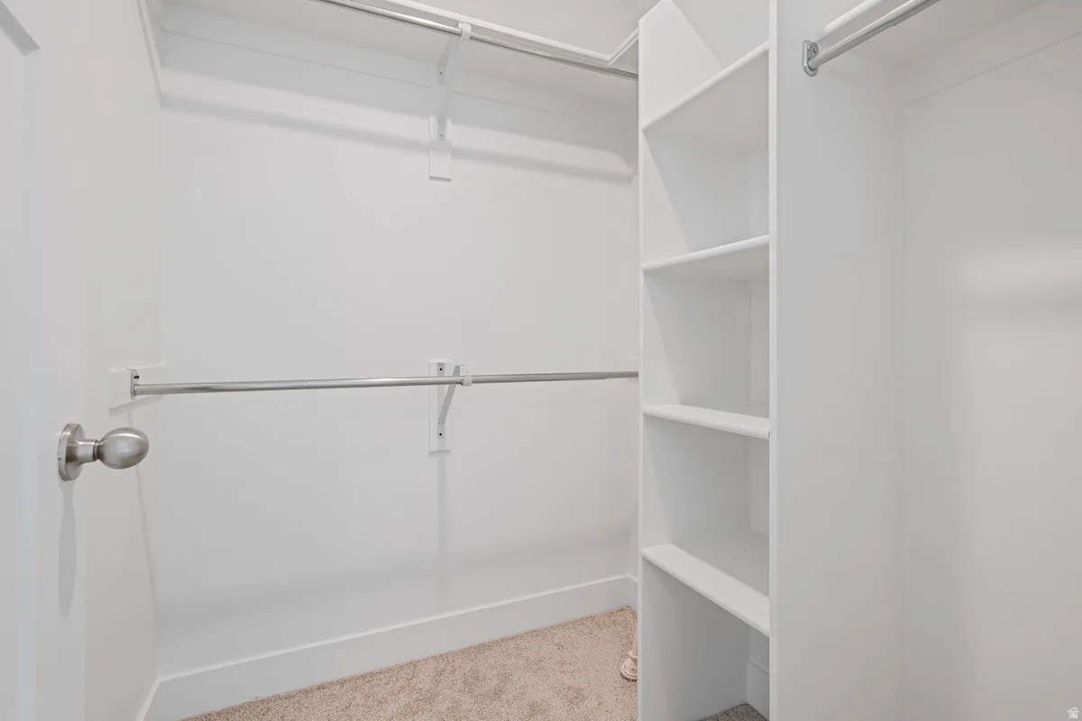Walk-in closet featuring built-in shelving, multiple hanging rods, white walls, and carpet flooring