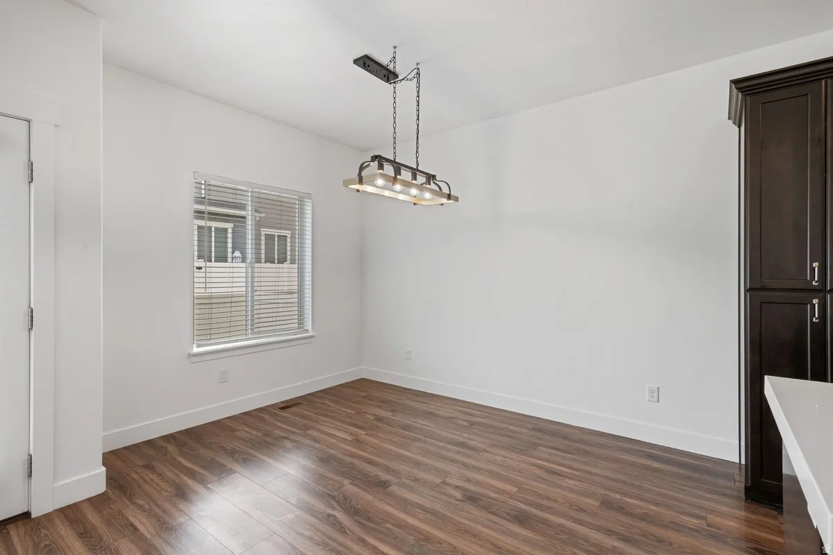 Spacious room featuring wood-finish flooring, white walls, and a contemporary linear chandelier