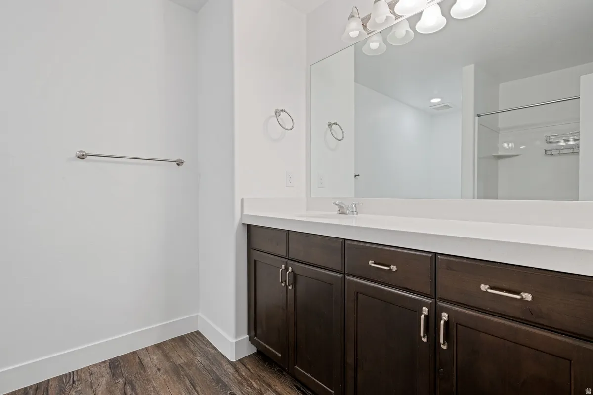 Bathroom featuring a dark wood-finish vanity with a light countertop, a spacious wall-mounted mirror, and overhead vanity lighting