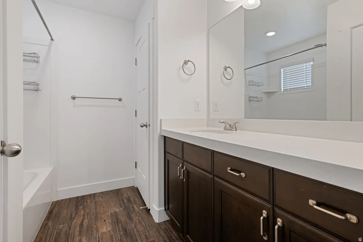 Bathroom featuring a dark wood-finish vanity with a light countertop and brushed nickel hardware, a large vanity mirror, and wood-finish flooring