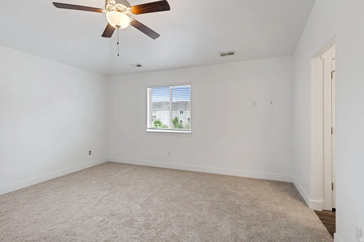 Bright interior room featuring a ceiling fan with integrated lighting, neutral-toned carpet, white walls, and a window with horizontal blinds