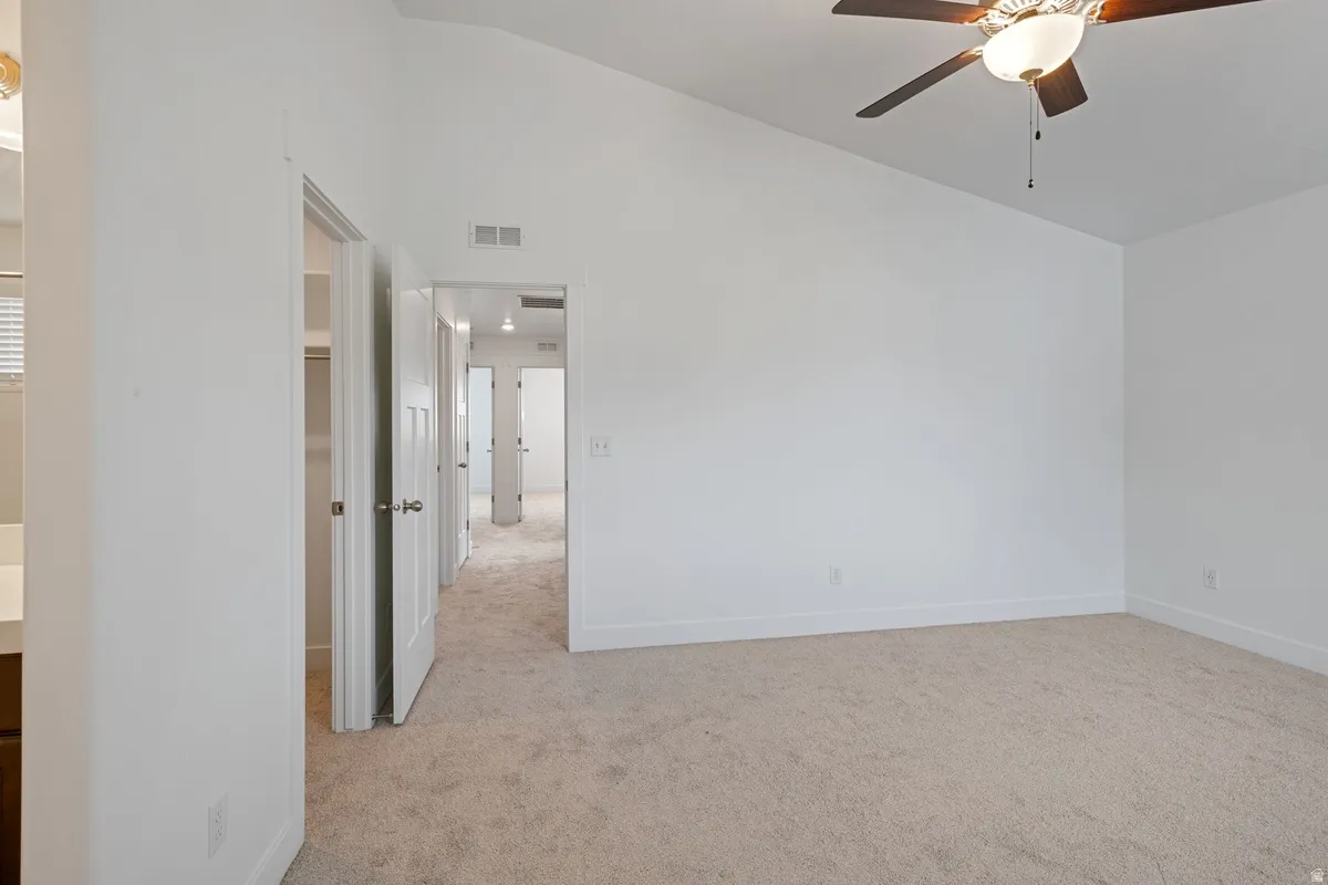 Spacious room featuring vaulted ceilings, light-colored carpeting, white baseboards, and a contemporary ceiling fan with integrated lighting