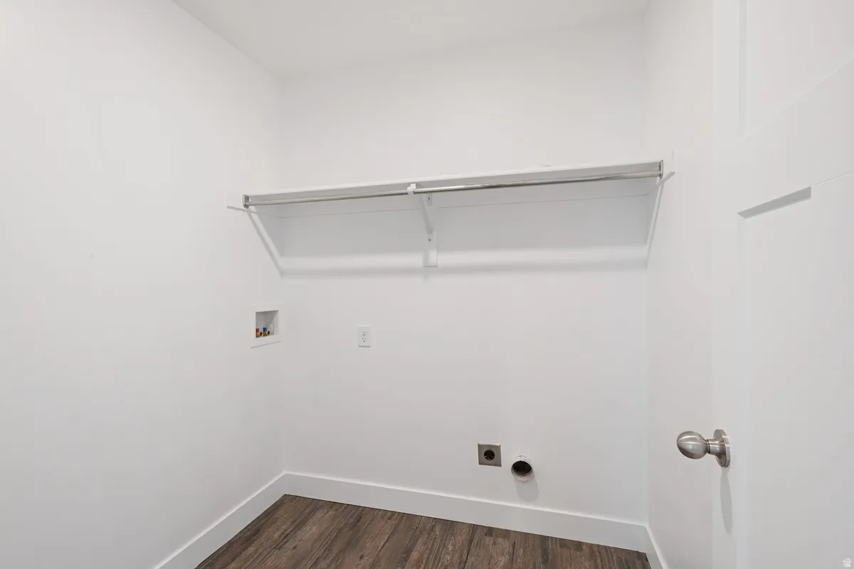 Laundry area featuring wood-finish flooring, white walls, and a built-in shelf with hanging rod