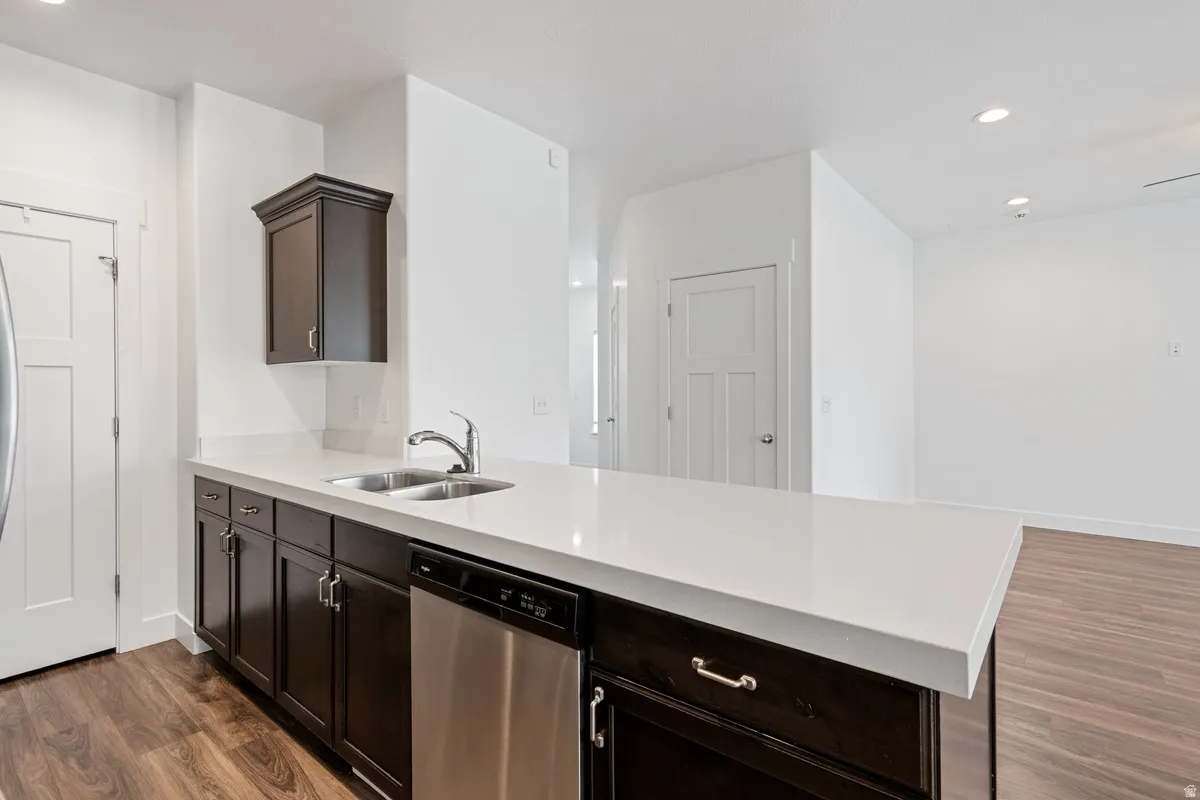 Kitchen island featuring a double basin stainless steel sink, stainless steel dishwasher, and dark wood-finish cabinetry