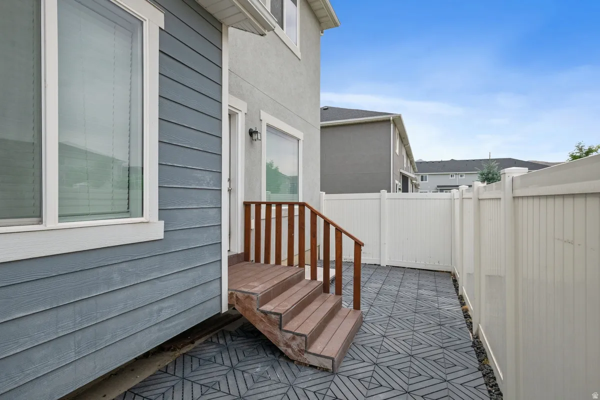 Rear patio featuring geometric pattern pavers, wood-finish steps with railing, and a white privacy fence
