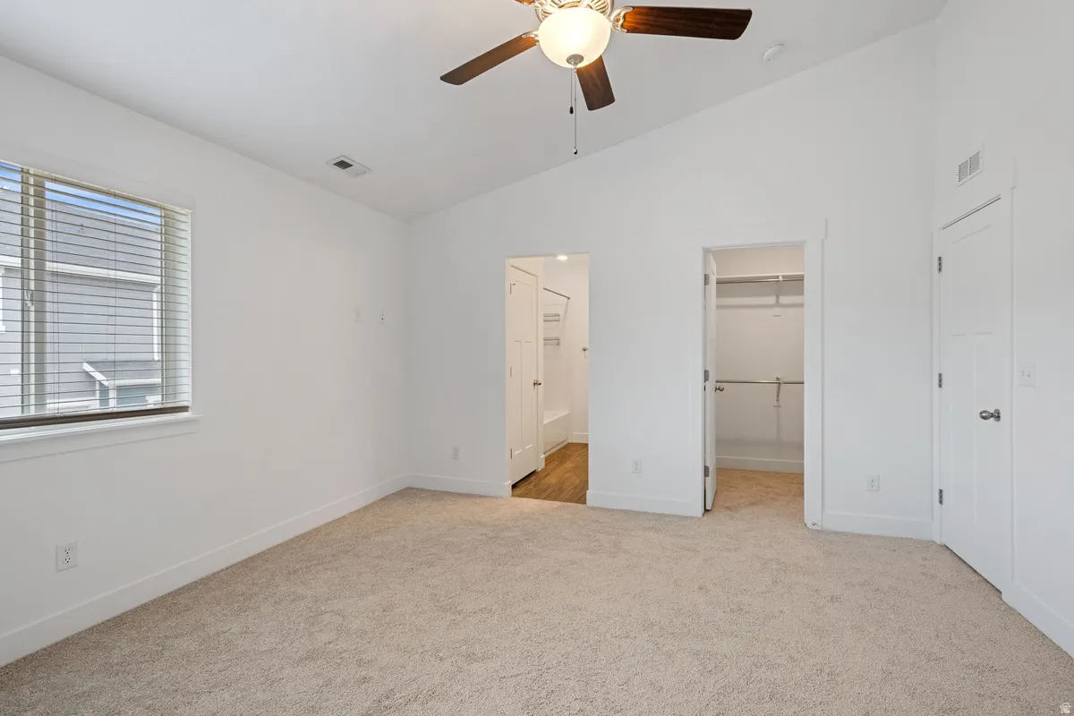 Spacious room featuring vaulted ceilings, neutral-toned carpeting, a ceiling fan with light fixture, and a window with horizontal blinds